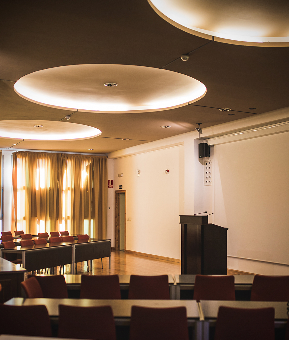 Salón de conferencias de la Escuela Técnica Superior de Ingeniería de Caminos, Canales y Puertos. Cuenta con un atril con micrófonos y mesas con asientos para el público.