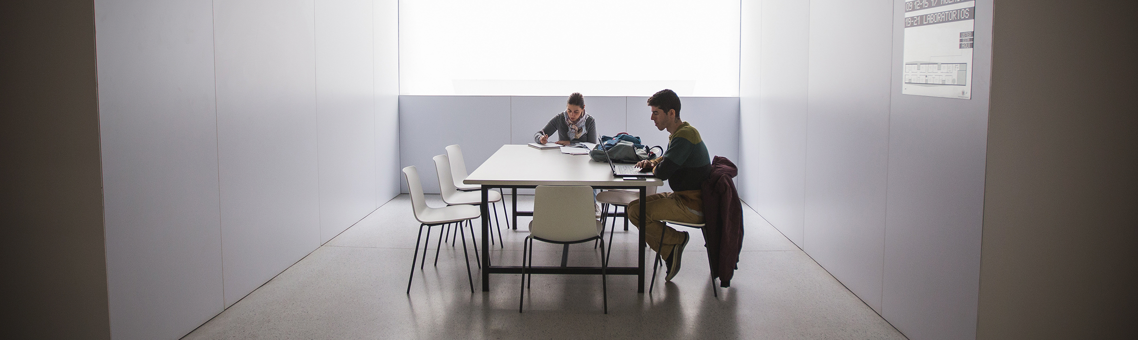 Dos estudiantes mirando apuntes en una mesa de estudio en el pasillo de la Facultad de Ciencias de la Salud