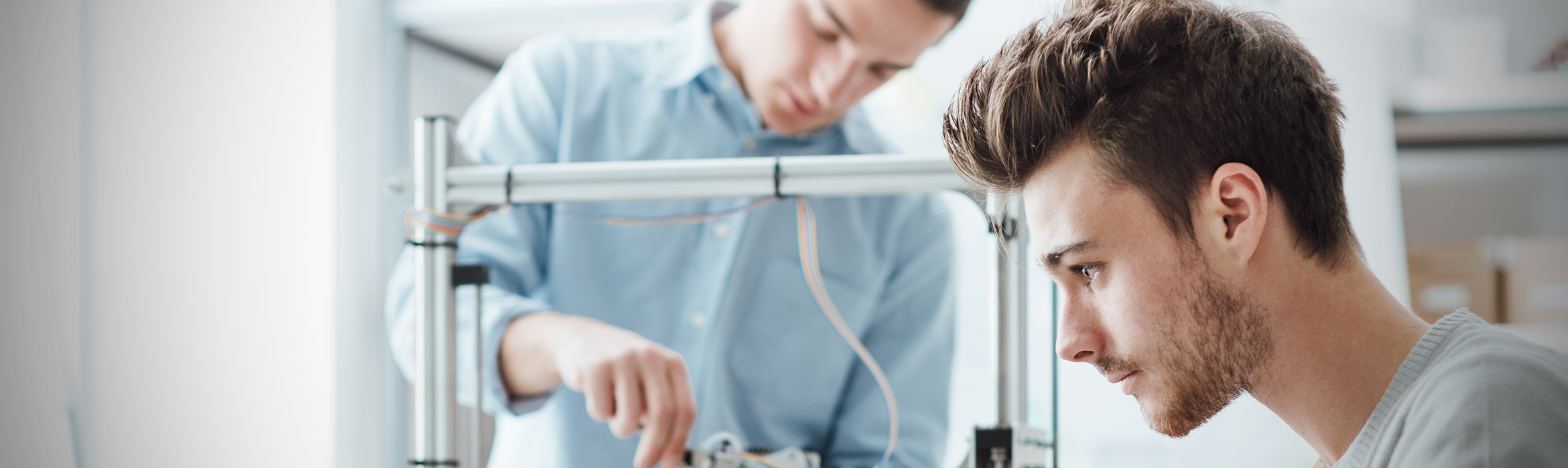 Un estudiante ajustando una impresora 3D mientras otro teclea en un ordenador portátil