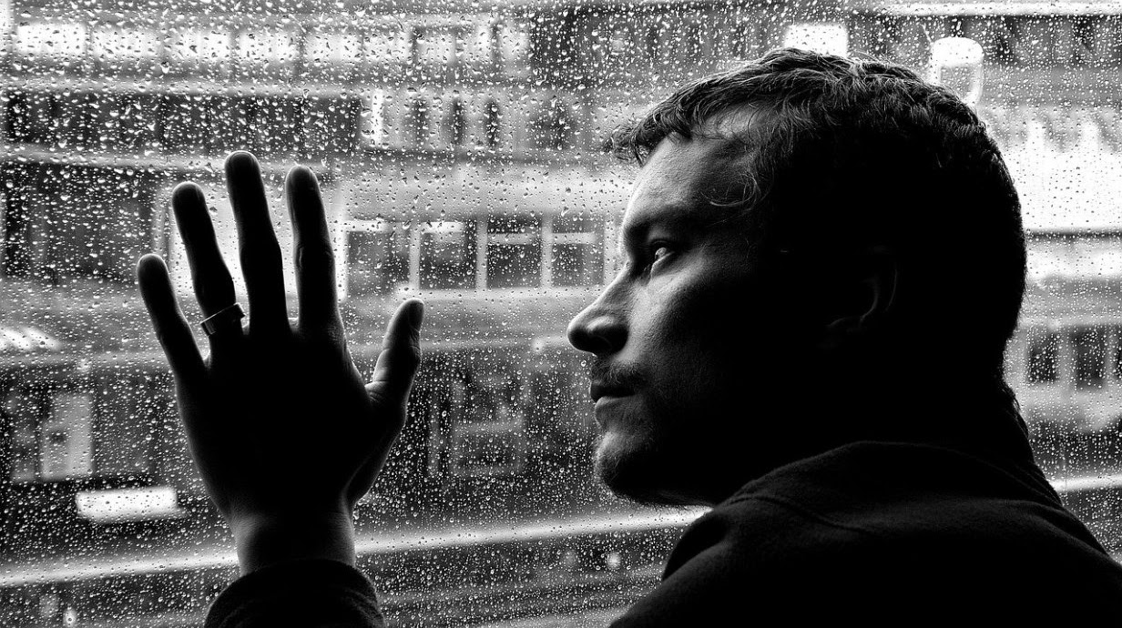Una persona mira por la ventana la lluvia caer. Imagen en blanco y negro.